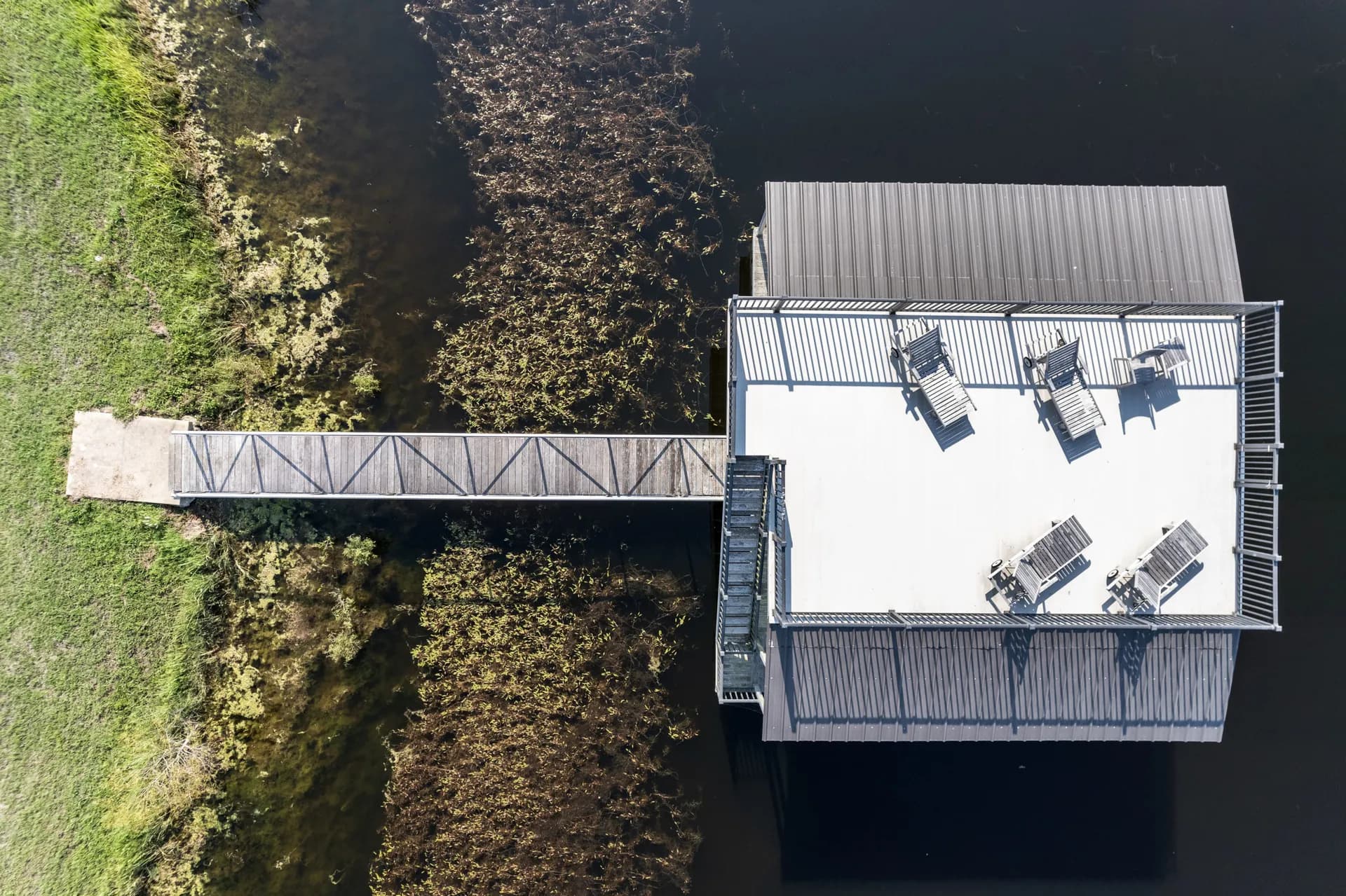 Overhead view of an aluminum covered dock and gangway with a furnished sun deck on a green pond