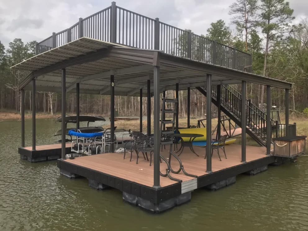 Close view of a two-story covered aluminum dock with a furnished lower deck, a boat lift, and stairs up to a railed sun deck